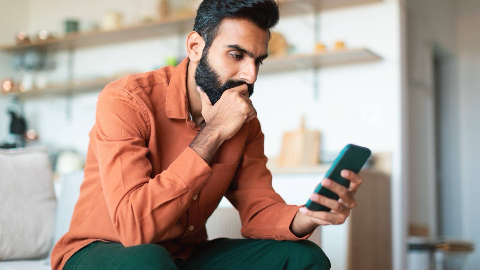 Man at home thinking while checking his phone