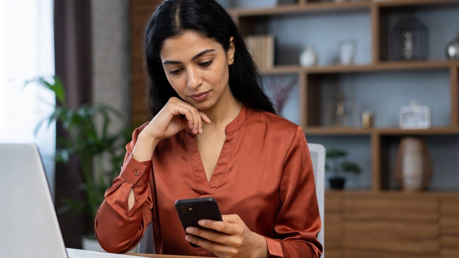 Woman at home thinking over a decision while checking her phone