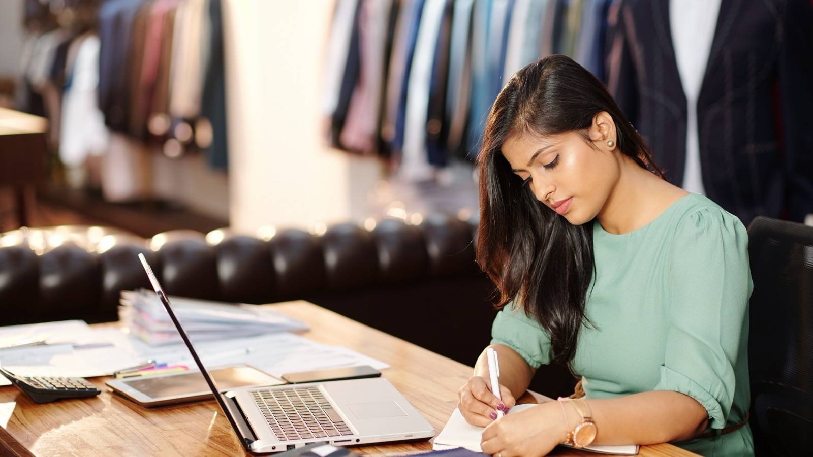 Small shop owner writing figures in a notebook at her desk