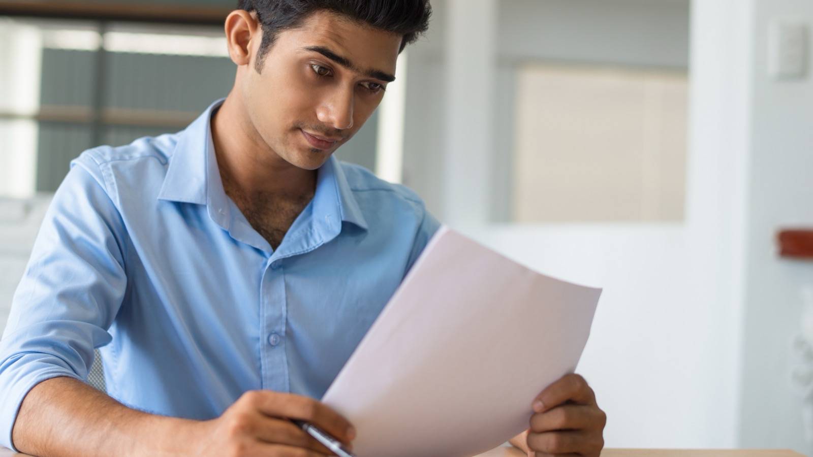 Man reading a document carefully, pen in hand