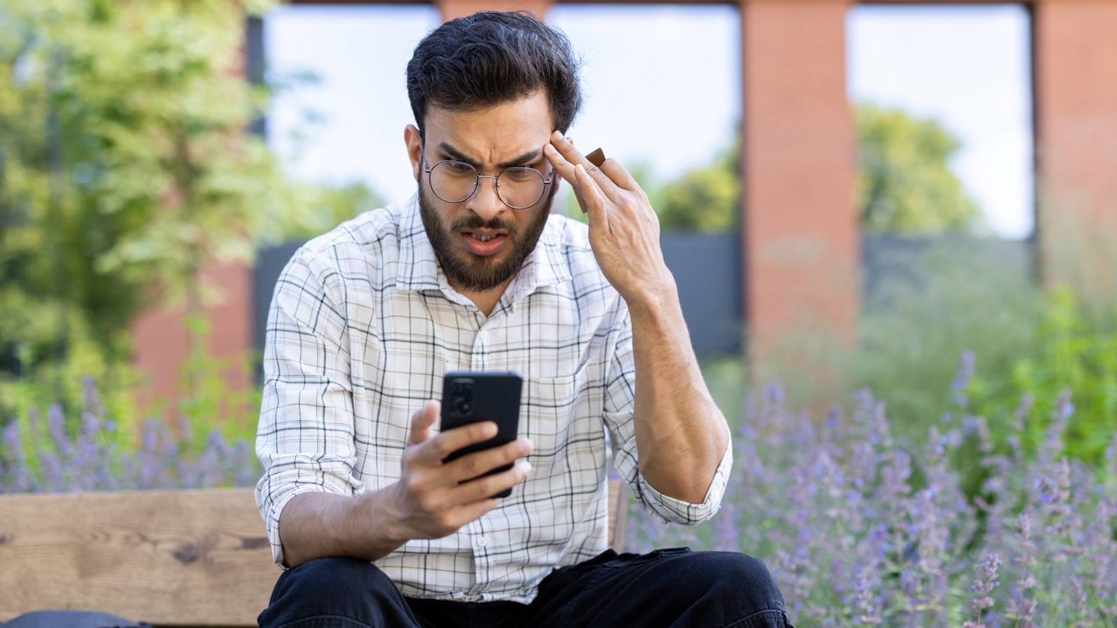 Man on a park bench frowning at a message on his phone
