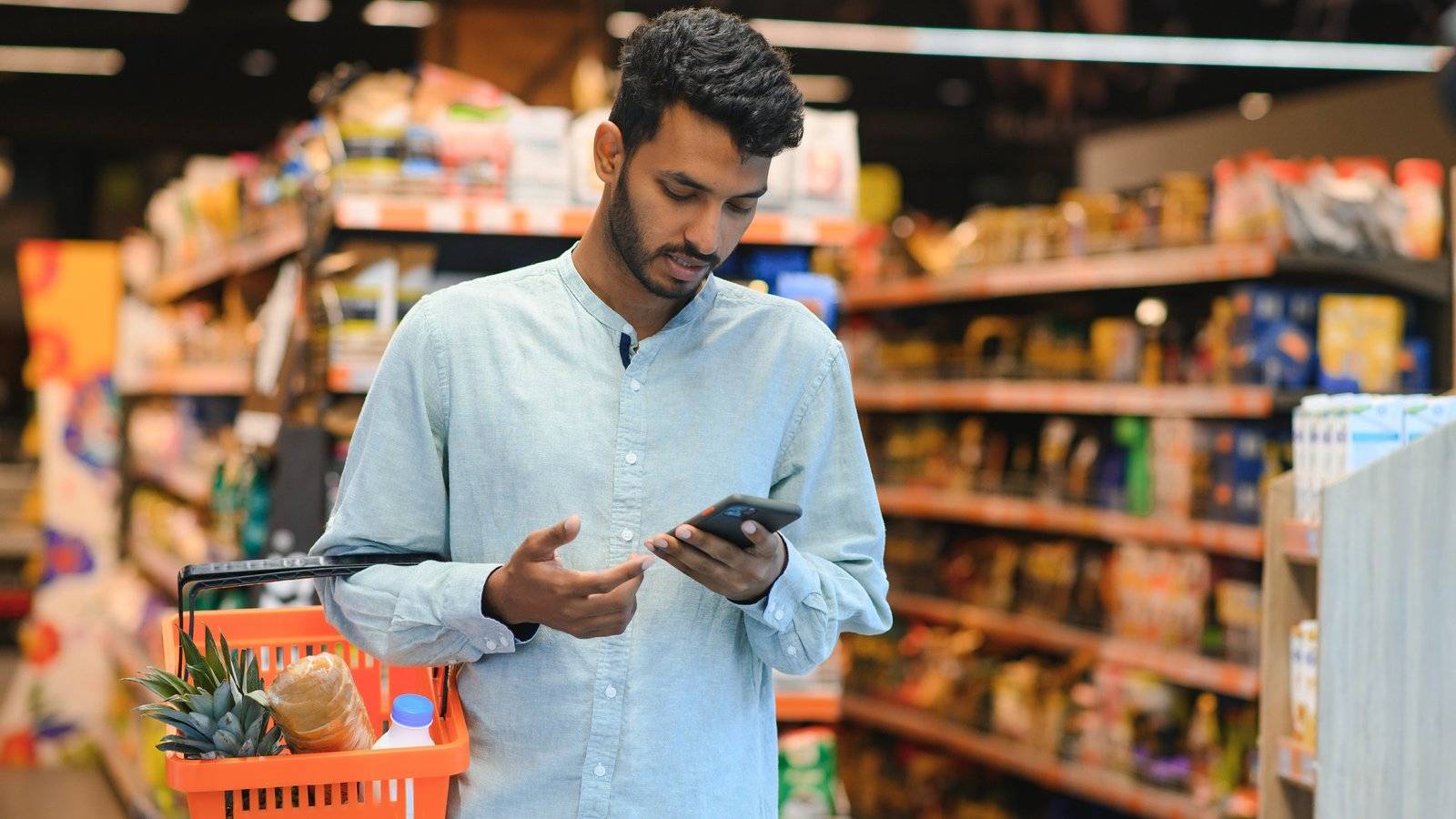 Young man with a shopping basket checking a payment on his phone in a shop
