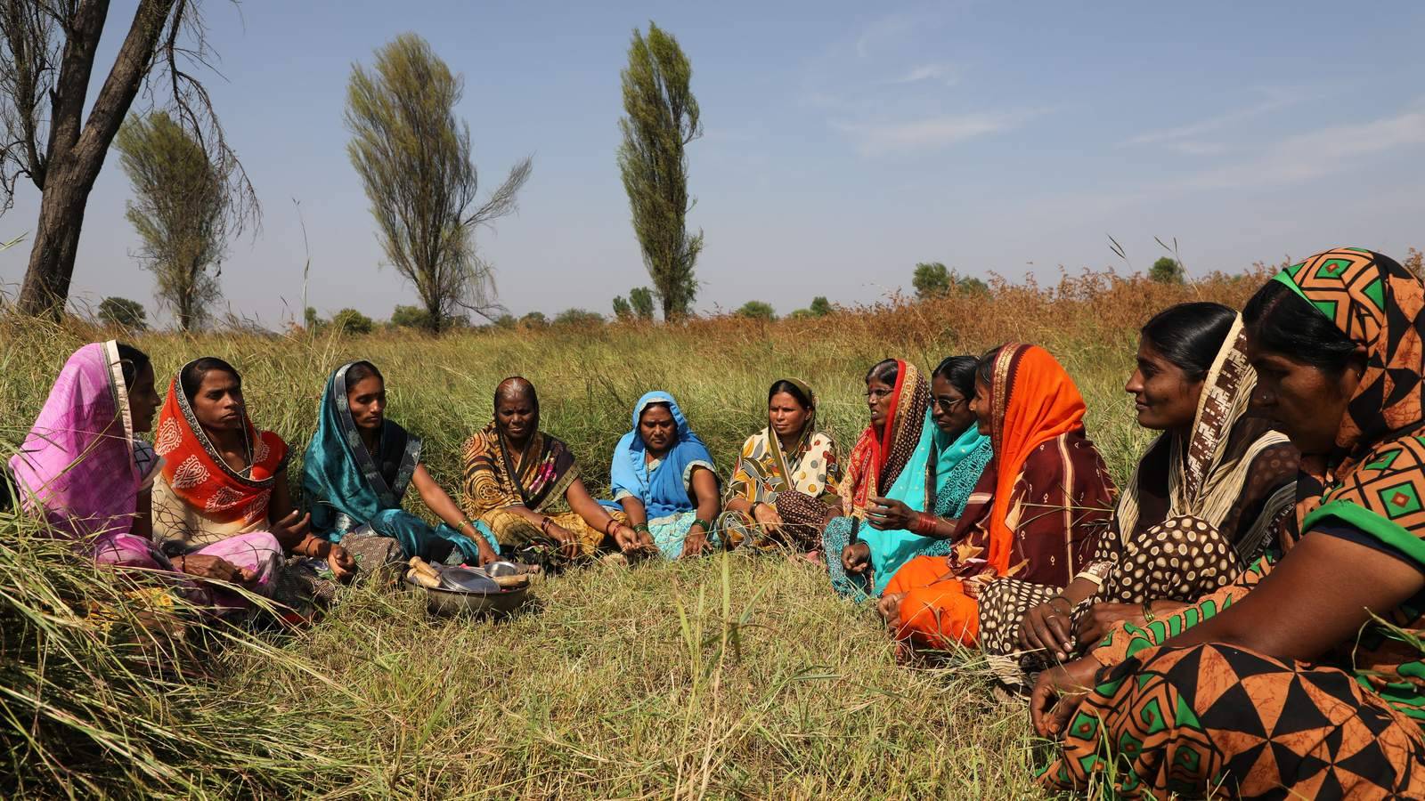 Village women sitting in a circle in a field, holding a meeting